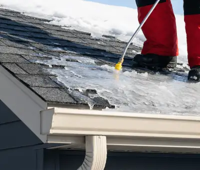 Ice dam removal technician using a steam wand to melt thick ice buildup on a residential roof in Lincoln, NE