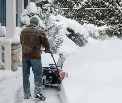 Residential snow removal technician using a snow blower to clear a home driveway and walkway in Lincoln, NE